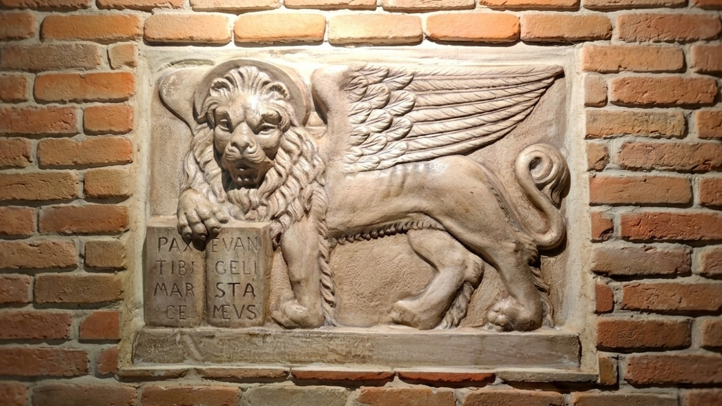 The famous winged lion statue atop a column in Piazza San Marco, with the Doge's Palace in the background at sunset.